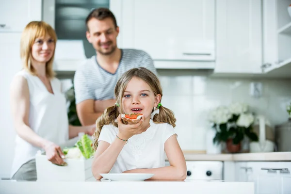 Pige spiser brød med tomat og purløg i køkkenet - Stock-foto