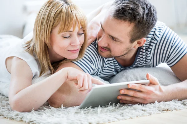 Casal com tablet deitado no chão e surfando na rede — Fotografia de Stock