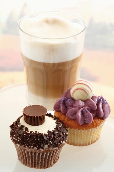 Nahaufnahme von Buttercreme-Cupcakes mit einem Glas Latte Macchiato — Stockfoto