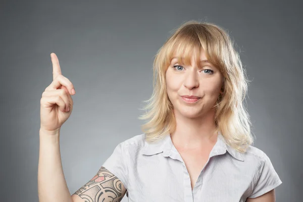 Junges Frauenporträt auf grauem Hintergrund, mit dem Finger zeigend — Stockfoto