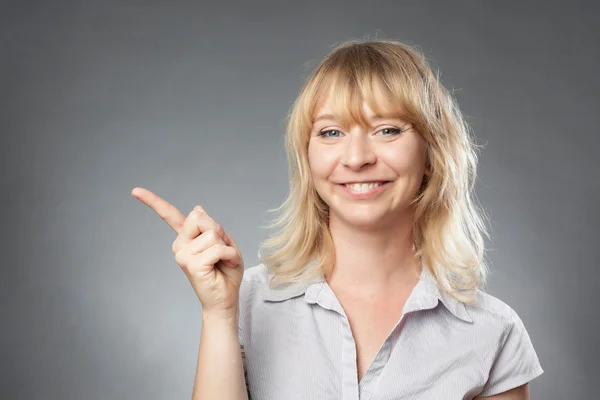 Young woman portrait on grey background, pointing with finger — Stock Photo, Image