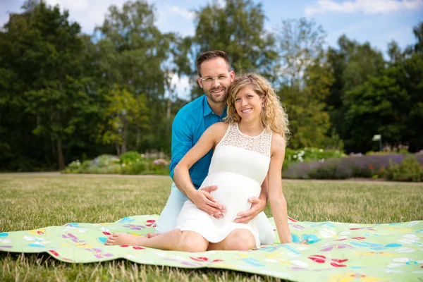 Pareja feliz esperando un bebé, sentado en una manta en el parque — Foto de Stock