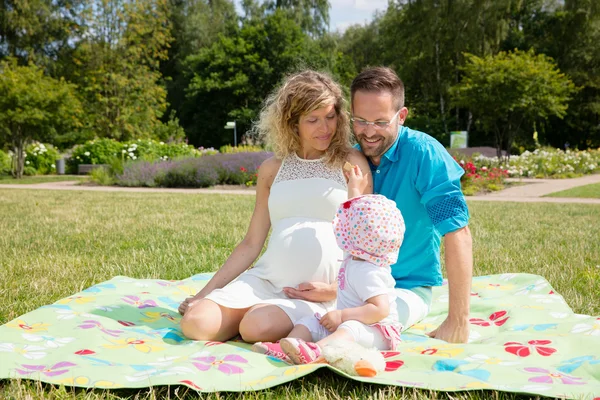 Feliz casal esperando bebê, sentado em cobertor no parque — Fotografia de Stock