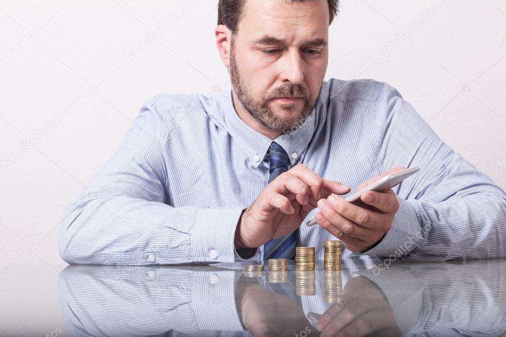 Mature man at desk with stacked euro coins using smart phone