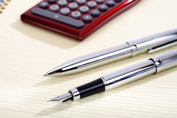 Ball-point, pen and pocket calculator lying on a sheet, close-up