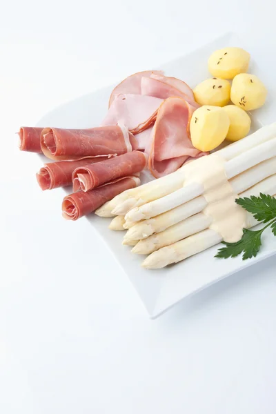 Спаржа, картофель, ветчина и петрушка в тарелке на белом спинке — стоковое фото