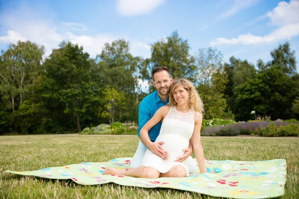 Pareja feliz esperando un bebé, sentado en una manta en el parque — Foto de Stock