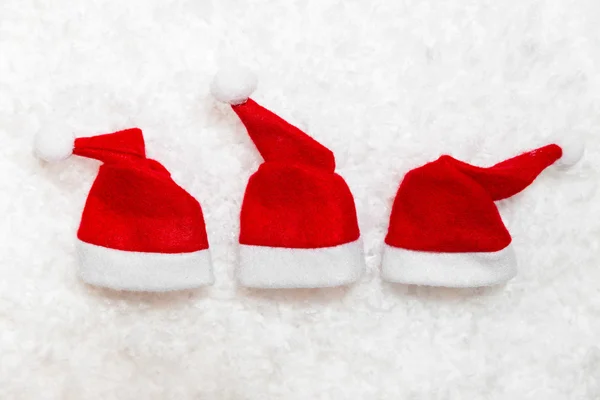Tre röda jultomten mössor i konstgjord snö — Stockfoto