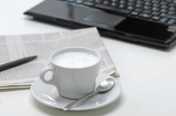 Zblízka na šálek kávy s novin a notebook v pozadí — Stock fotografie