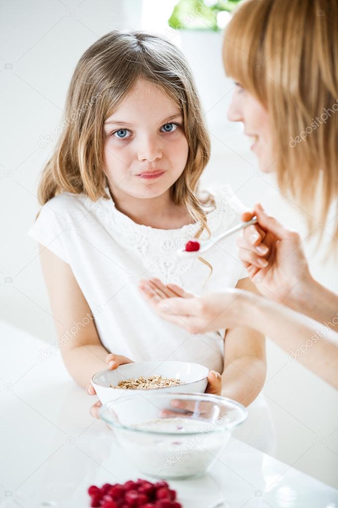 Mother feeding daughter with muesli and raspberries