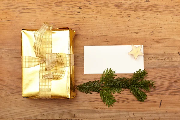Golden christmas present and blank card on wood — Stock Photo, Image