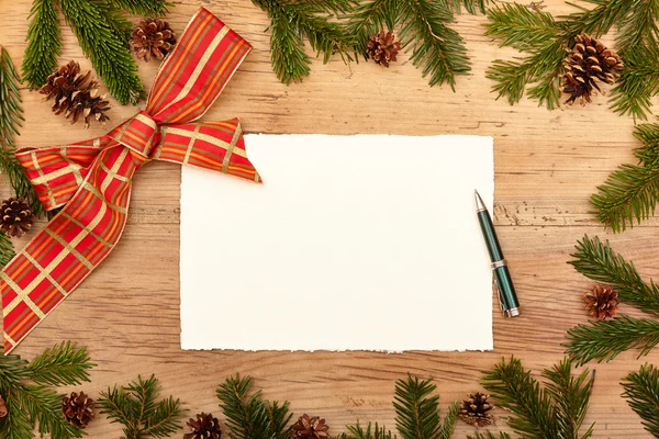 Ribbon, fir twigs and cones on wood, empty card and ballpen — Stock Photo, Image