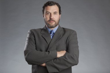 Gri arka planı katlanmış elleriyle ayakta ciddi iş adamı