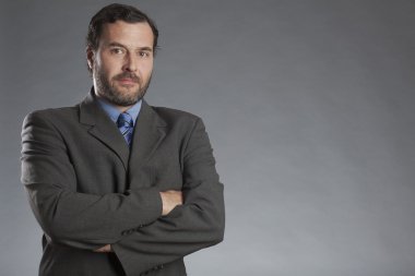 Gri arka planı katlanmış elleriyle ayakta ciddi iş adamı