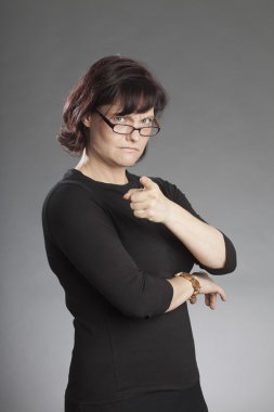 Mature brunette woman wearing glasses standing against gray background clipart