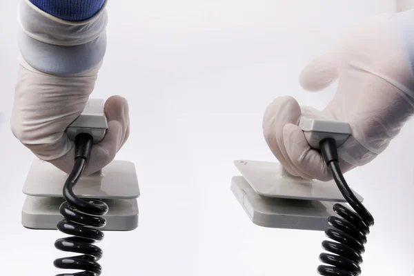 Manos en guantes protectores sosteniendo el desfibrilador sobre fondo blanco —  Fotos de Stock