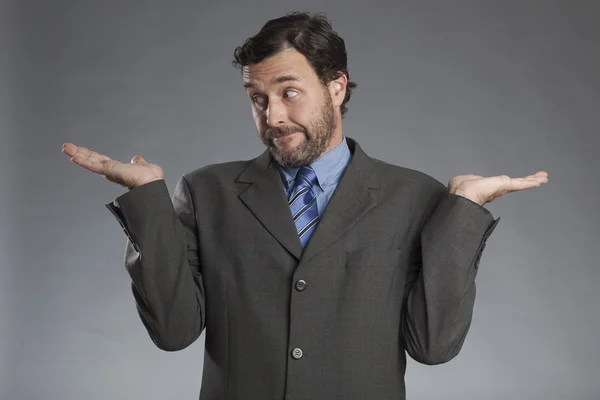 Skeptical businessman with both palms upwards against gray background — Stock Photo, Image