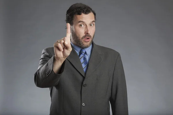 Zakenman houden wijsvinger tegen de grijze achtergrond — Stockfoto