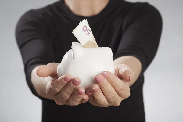 Woman holding piggy bank against gray background — Stock Photo, Image