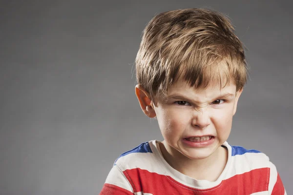 Молодий хлопчик виглядає сердитим, стискаючи зуби на сірому фоні — стокове фото