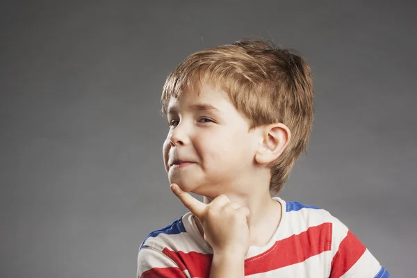 Ung gutt som ser omtenksom, smilende ut, med haken mot grå bakgrunn – stockfoto