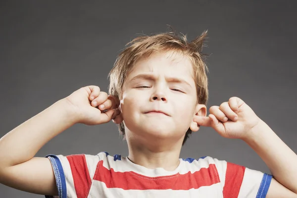 Mladý chlapec pokrývající uši proti šedé pozadí — Stock fotografie