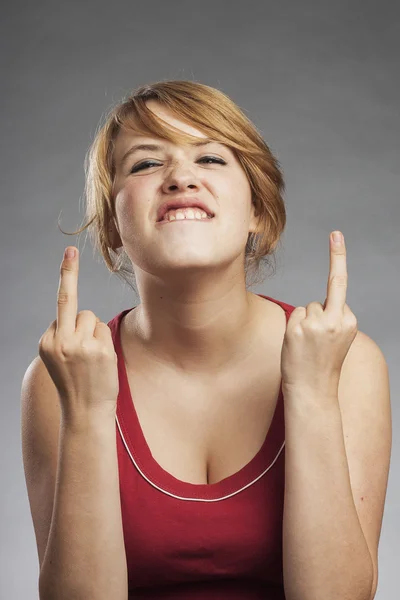 Teenage girl in red tank top showing obscene gesture against gray background — Stock Photo, Image