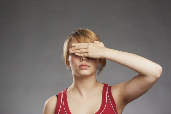Teenage girl in red tank top covering eyes against gray background — Stock Photo, Image