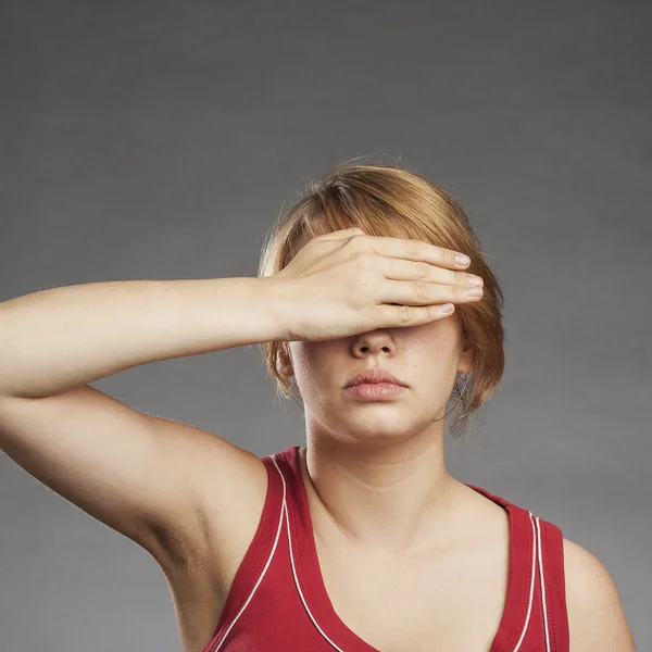 Девочка-подросток в красной майке закрывает глаза на сером фоне — стоковое фото