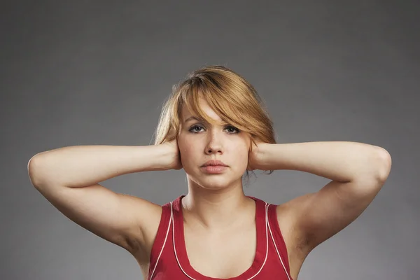 Adolescente chica en rojo tanque superior cubriendo las orejas contra el fondo gris — Foto de Stock