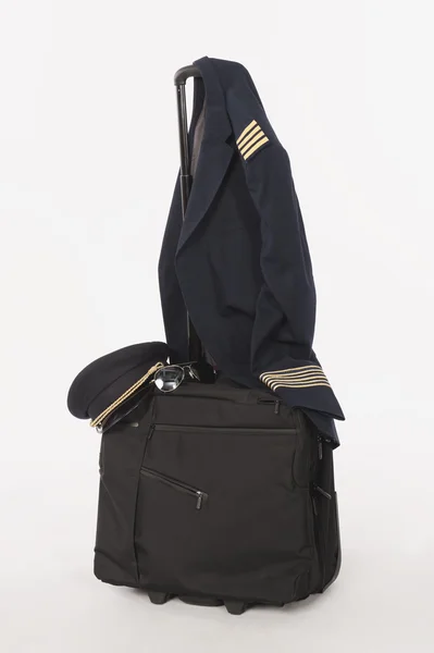 Flugbegleiter-Uniform und Hut hängen am Rollgepäck auf weißem Hintergrund — Stockfoto
