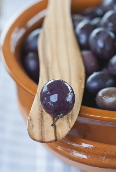 Italy, Tuscany, Magliano, Close up of black olives in bowl with one olive on wooden spatula — Stock Fotó