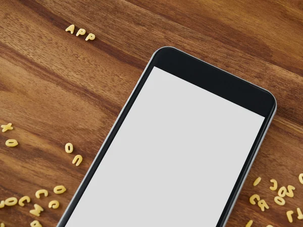 Smartphone on wood, alphabet noodles — Stock Photo, Image