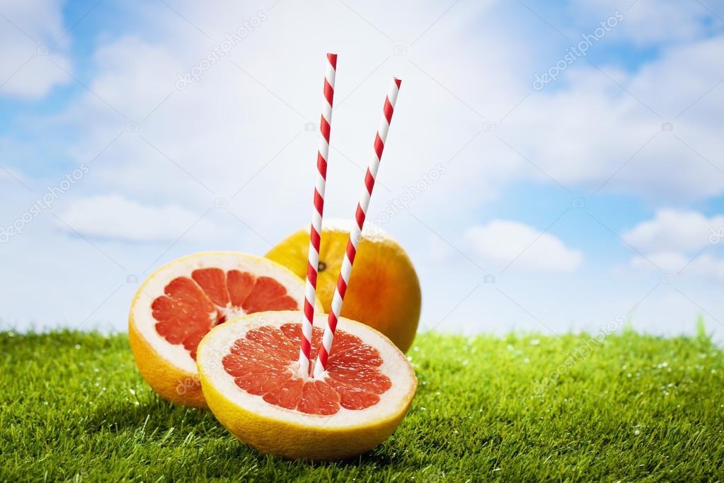 Grapefruits on grass, drinking straws