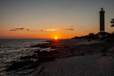 Kayalık denizde gün batımında deniz feneri, Yunan