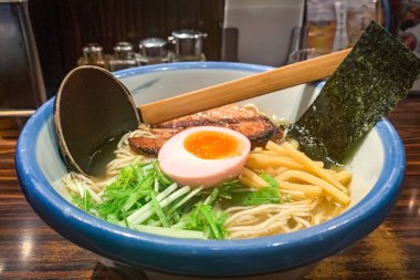 Mavi kase Japon eriştesi, yarım yumurta, et, sebze ve yosun ile ahşap masada. 