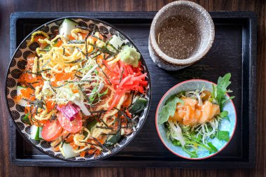 Bir kase sebze salatası ve siyah ahşap tepside çay.