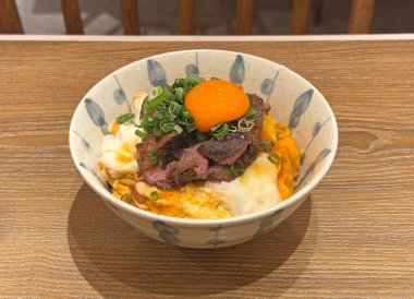 Tahta bir masada çiğ yumurta sarısı ve yeşil soğanlı leziz et kasesi.