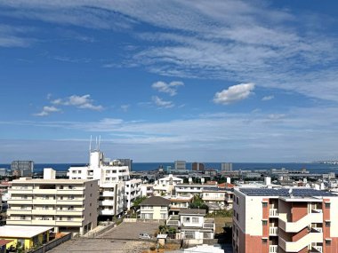 Geniş açı, çeşitli yerleşim birimlerine ve ufka uzanan engin mavi okyanusa sahip yoğun şehir manzarasını parçalı bulutlu bir gökyüzünün altında yakalar.