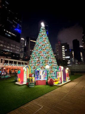 Hong Kong 'da renkli dekorasyon ve hediye kutularıyla çevrili canlı bir şehir manzarasının ortasında duran büyük, parlak bir Noel ağacı büyülü bir tatil atmosferi yaratıyor.