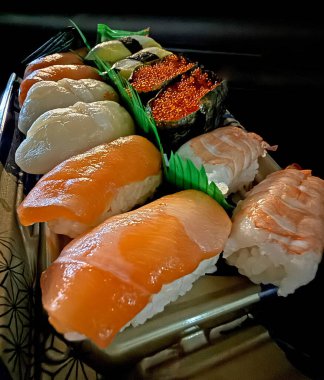 Somon, karides ve tobiko da dahil olmak üzere çeşitli nigiri suşi parçalarının yakın çekim görüntüsü, paket servis konteynerinde sunuluyor.