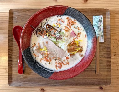 Buharlı bir tonkotsu ramen kasesinin yakın çekim görüntüsü kremalı çorbasını, leziz domuz dilimlerini ve narin garnitürlerini gözler önüne seriyor.