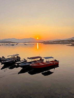 Altın saat, sakin denizi yansıtan ılık renkler ile gökyüzünü boyar. Kıyıya yakın kıyıda huzur içinde duran küçük tekneler gibi.