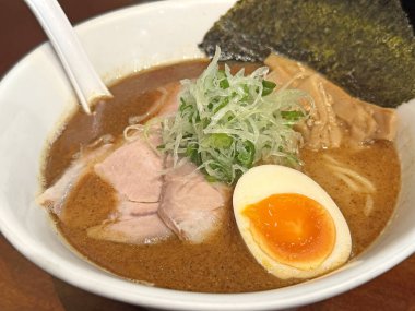 Beyaz bir kasede servis edilen zengin bir tonkotsu ramen yemeğinin yakın çekim görüntüsü, yumuşak chashu domuz eti dilimleri, mükemmel pişirilmiş bir jitama yumurtası, nori deniz yosunu ve menma bambu filizleri