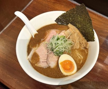 Beyaz bir kasede servis edilen zengin bir tonkotsu ramen yemeğinin yakın çekim görüntüsü, yumuşak chashu domuz eti dilimleri, mükemmel pişirilmiş bir jitama yumurtası, nori deniz yosunu ve menma bambu filizleri