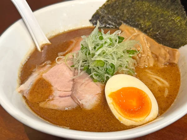 Beyaz bir kasede servis edilen zengin bir tonkotsu ramen yemeğinin yakın çekim görüntüsü, yumuşak chashu domuz eti dilimleri, mükemmel pişirilmiş bir jitama yumurtası, nori deniz yosunu ve menma bambu filizleri