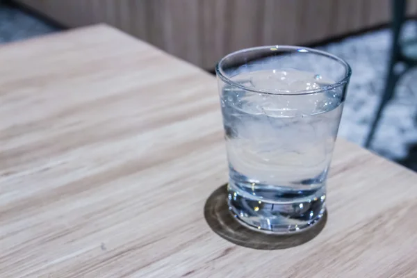 Glass of cool water with ice on wooden table inside restaurant Stock Photo