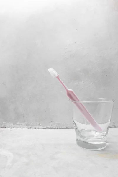 Cepillo de dientes rosa dentro de vidrio transparente con fondo de hormigón —  Fotos de Stock