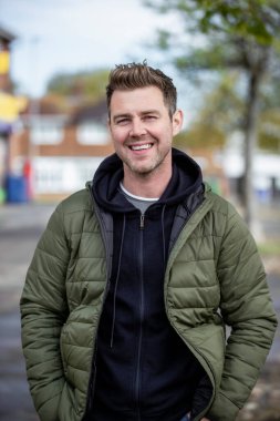 Orta yaşlı beyaz bir adamın günlük giysiler giymiş bir portresi. Gülümsüyor ve kameraya bakıyor..