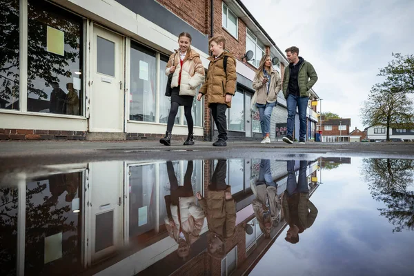 A shot of a four person family walking along a street pathway, the parents are taking their children home from school.